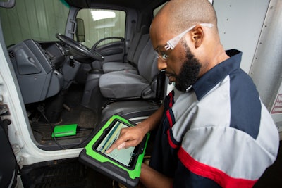 A man uses a green Bosch diagnostic tablet on a truck.