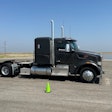 A gray Peterbilt truck without a trailer in front of a wet pad of asphalt.