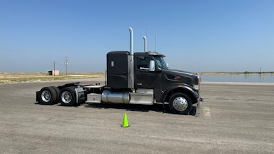 A gray Peterbilt truck without a trailer in front of a wet pad of asphalt.