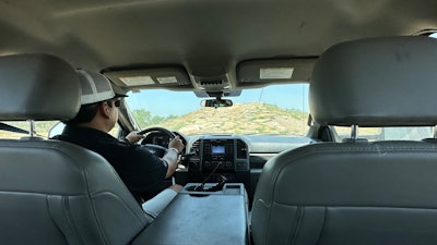 A man in a black shirt and white cap drives a truck up a steep hill of boulders.
