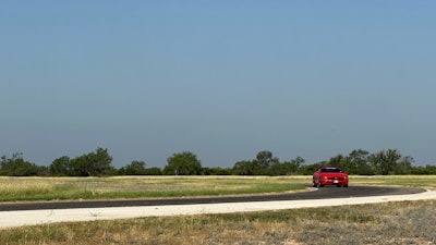 A red Mustang convertible takes a corner on a dry race track.