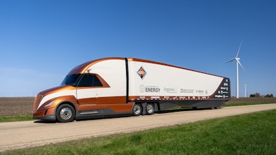 An orange and white Class 8 truck by Navistar with a trailer that has logos on it.
