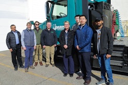 A group of men standing in front of a teal truck.