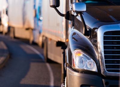 A row of heavy trucks and trailers lead by a black truck.