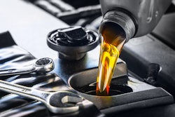 A bottle of engine oil being poured into an engine with a wrench nearby.