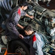 Two technicians work under the hood of a truck.