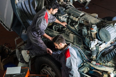Two technicians work under the hood of a truck.