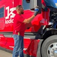 A man in a red shirt and jeans adjusts a part on the side of a bright red Kodiak autonomous Class 8 truck.
