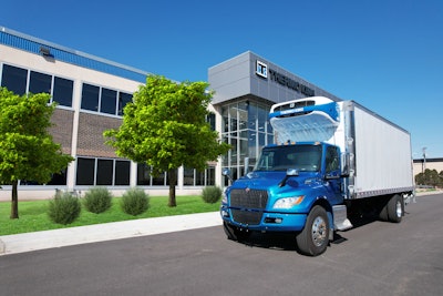 A blue truck with a refrigerated trailer parked in front of a building.