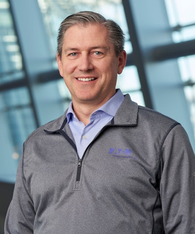 A man in an Eaton-branded gray pullover and blue business shirt.