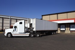 A truck with a refrigerated trailer outside of a warehouse.
