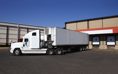 A truck with a refrigerated trailer outside of a warehouse.