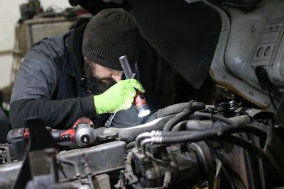 A man uses a flashlight to examine a piece of equipment at JE-CO.