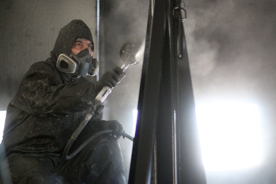 A masked and hooded tech does body work at JE-CO.