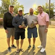 Two men holding awards standing with two other men outdoors at dusk.