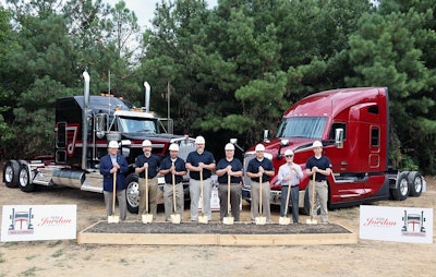 Eight people with shovels stand in front of a box of dirt and two Class 8 trucks.