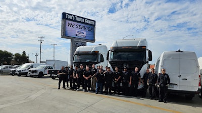 Tom's Truck Center team in front of sign and trucks