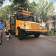 A man holds a child's hand as they walk away from a school bus.