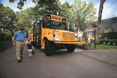 A man holds a child's hand as they walk away from a school bus.