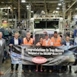 A group of people in suits and orange safety vests stand in front of a truck. They are holding a banner with the Peterbilt logo and the Massey Motor Freight Logo. It reads, 'Congratulations to Troy Massey, recipient of the 100,00th Model 389'