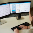 A woman sits at a desk looking at two computer screens with fleet data displayed by TracKing Pro telematics.