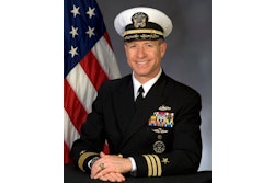 A man in a Navy uniform in front of a flag.
