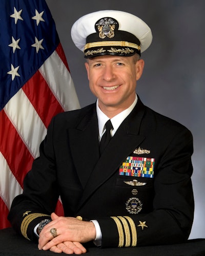 A man in a Navy uniform in front of a flag.