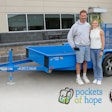 A man and woman stand in front of a blue trailer.