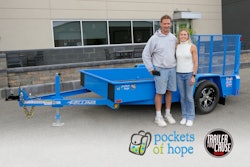 A man and woman stand in front of a blue trailer.