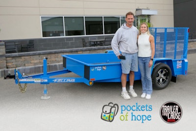 A man and woman stand in front of a blue trailer.