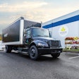 A black medium duty Freightliner eM2 box truck sits in front of a distribution center.