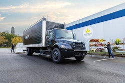 A black medium duty Freightliner eM2 box truck sits in front of a distribution center.