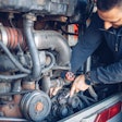 A truck technician works under a hood.