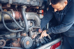 A truck technician works under a hood.