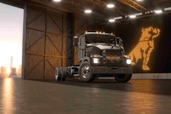 A dark gray electric Mack medium-duty truck in front of a Mack logo.