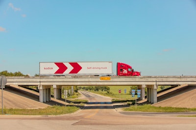 A white-and-red truck and trailer crosses an overpass under a blue sky.