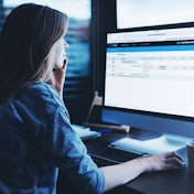 A woman sits at a computer displaying a telematics dashboard.
