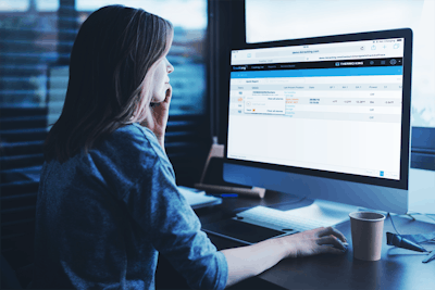 A woman sits at a computer displaying a telematics dashboard.