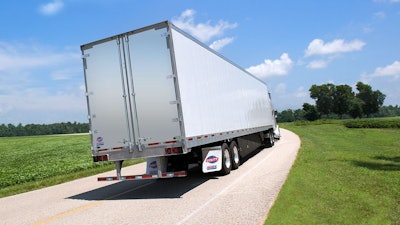 A truck pulling a Utility dry van trailer down a road surrounded by green trees and grass.