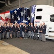 A group of people in matching suit coats stand in front of a specially marked Volvo truck.