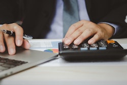 A man works on a calculator and laptop