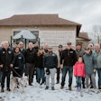 A group of people stands in the snow in front of a community center.