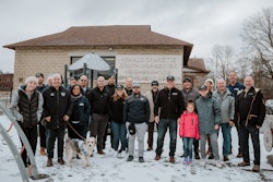 A group of people stands in the snow in front of a community center.