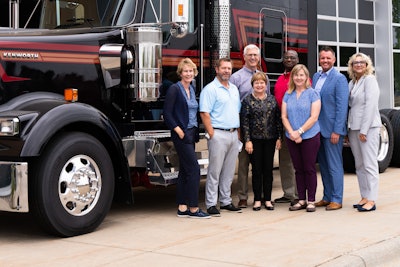 A group of people stand next to a new Kenworth truck.