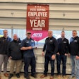 Six men stand around a flag that says 'Pete DePina Employee of the Year winner' with the ATG logo.