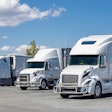 Three white trucks parked in a lot on a sunny day