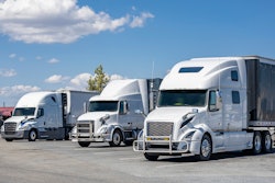 Three white trucks parked in a lot on a sunny day