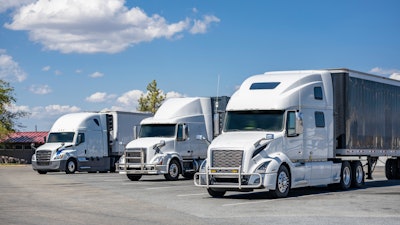 Three white trucks parked in a lot on a sunny day