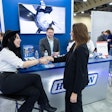 Two people shake hands on a trade show floor.