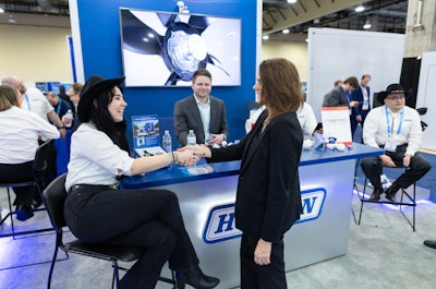 Two people shake hands on a trade show floor.